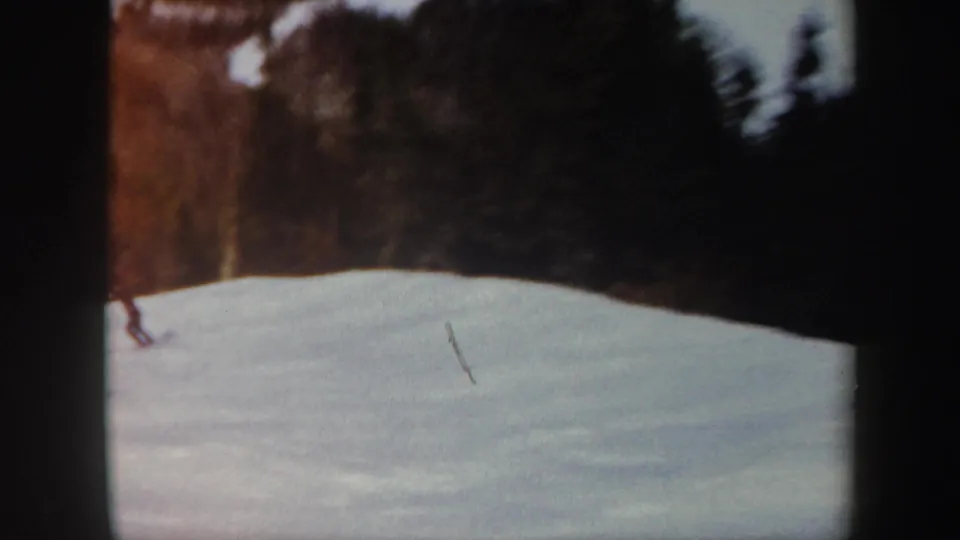 1962 Vermont 8mm frame showing a lone distant skier on a snow-covered slope bordered by winter woods.