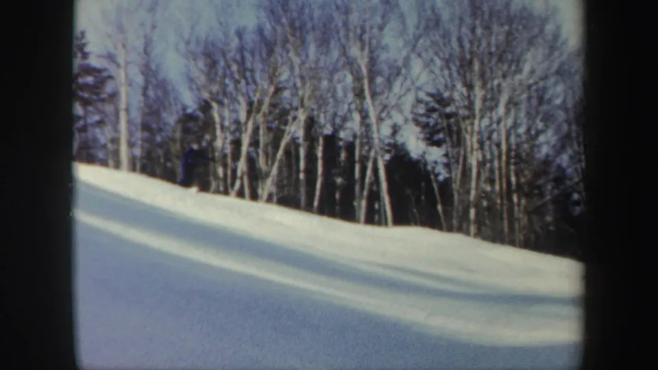 1962 Vermont 8mm view of a quiet ski slope with bare trees, evergreens, and long shadows across the snow.
