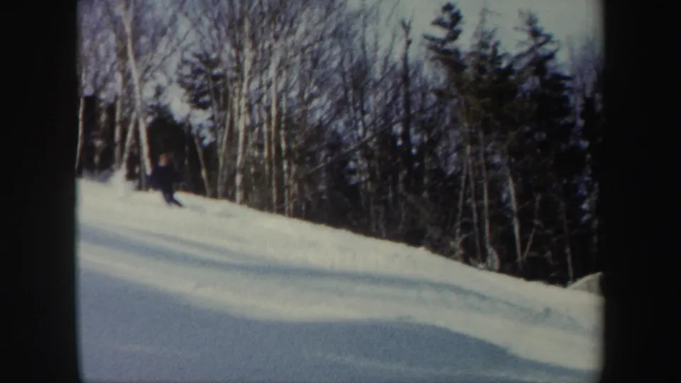 1962 Vermont 8mm frame with a lone skier turning on a snow-covered hillside below leafless trees and evergreens.
