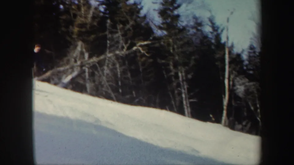 The skier passes near the left edge of the frame on a snowy wooded hill in Vermont home-movie footage.