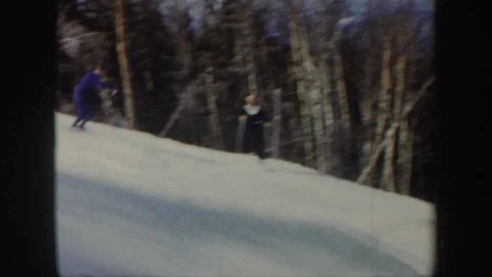 A skier continues downhill on a Vermont snow slope as another distant figure stands near the trees.