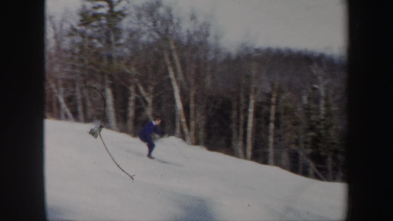 1962 Vermont home-movie frame showing a skier in blue on a snow-covered hillside bordered by birch trees and evergreens.