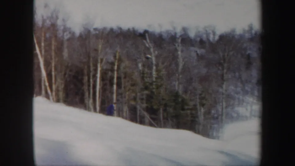 The blue-suited skier appears lower on the Vermont hillside, partly framed by snowbanks and winter trees.