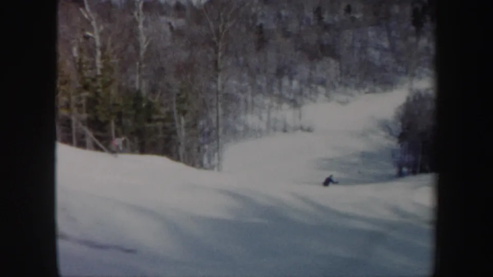 The skier nears the lower right of the snowy Vermont slope, framed by forest and the soft exposure of vintage 8mm film.