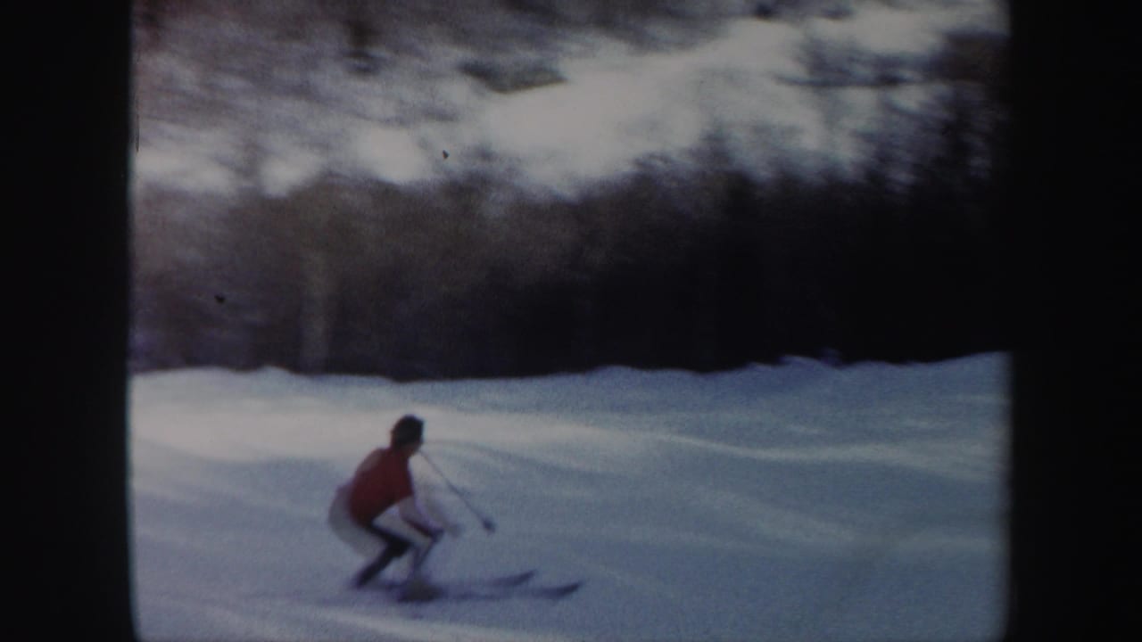 Skier in a red jacket crouches on a snowy downhill slope.