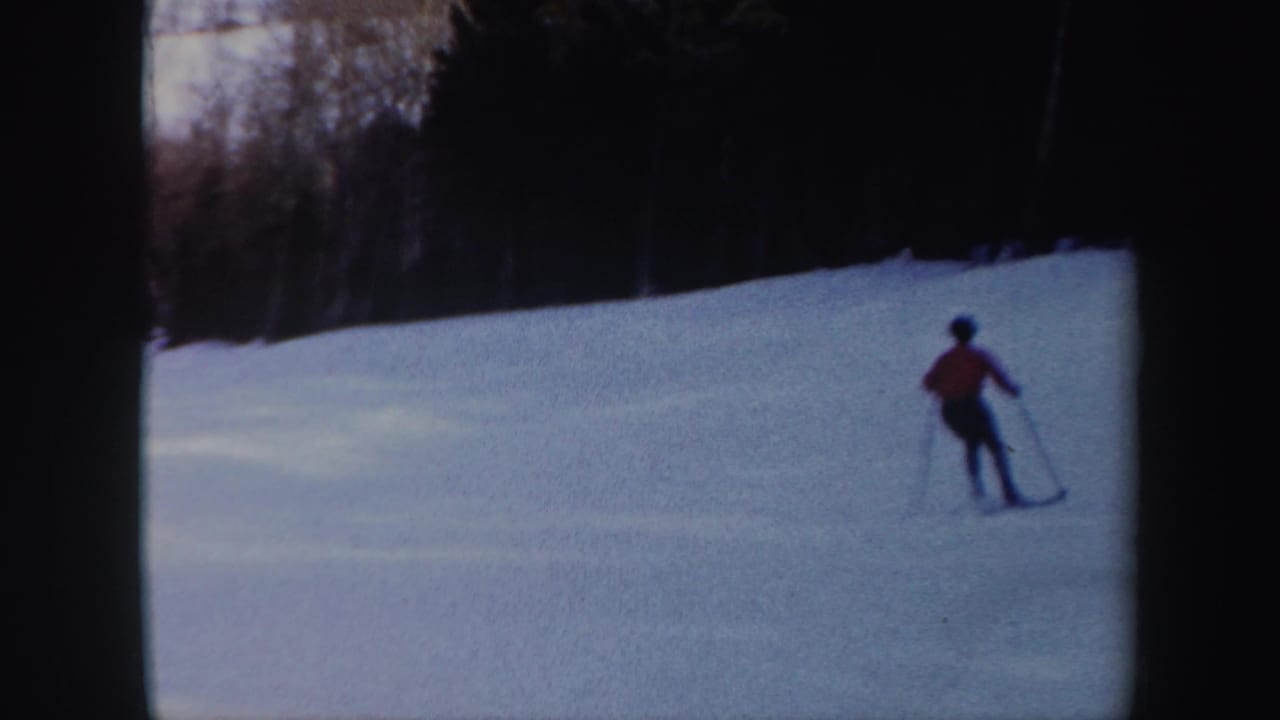 Skier in red moves across an open snowy slope near trees.