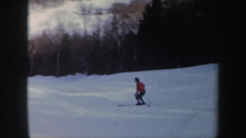The skier in a red jacket glides downhill on a Vermont snow slope, seen in soft 1962 8mm color footage.