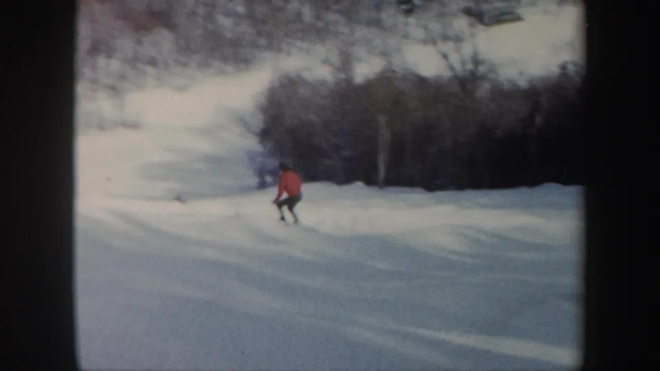 A red-jacketed skier turns on the snow below winter trees in Vermont 1962 home-movie footage.