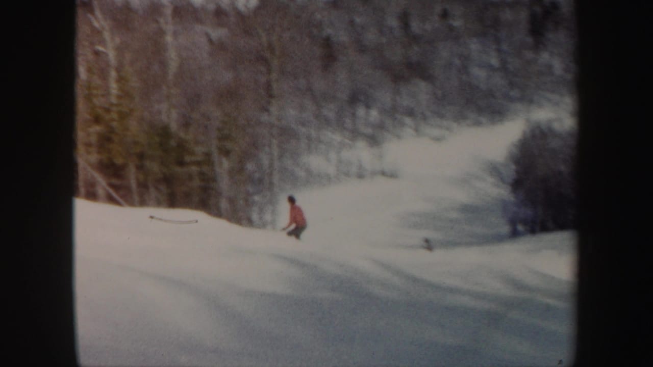 Adult skier in a red jacket moves down a snow-covered Vermont slope in 1962 home-movie footage.
