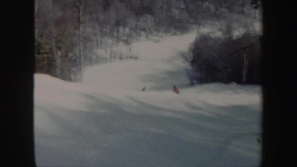 1962 Vermont 8mm frame showing a snowy slope with distant skiers, bare trees, and dark film gate edges.