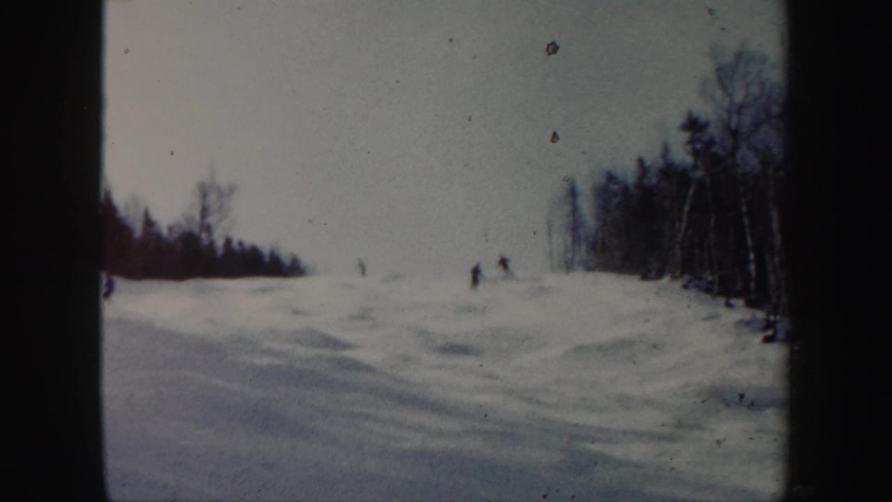 Open snowy hillside with small skiers near the upper right tree line.