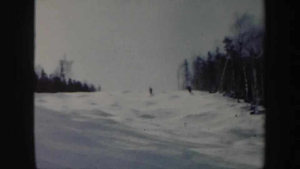 1962 Vermont 8mm frame showing two distant skiers descending a broad snowy slope beside a winter tree line.
