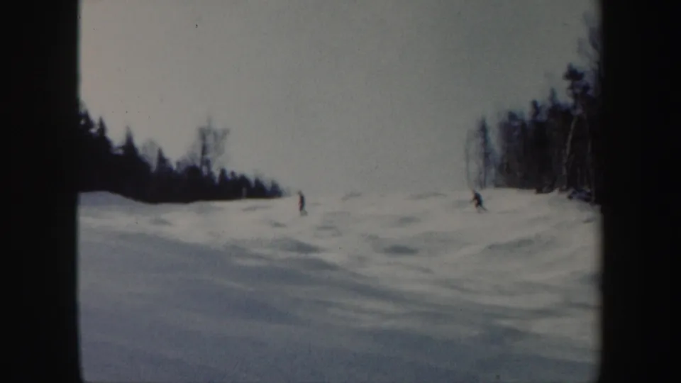 1962 Vermont 8mm frame with two skiers spaced across a snowy hillside near bare trees and a dark tree line.