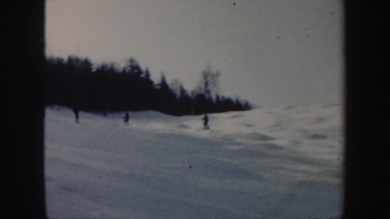 Small figures ski across a pale Vermont snow slope in a soft 1962 8mm home-movie frame.