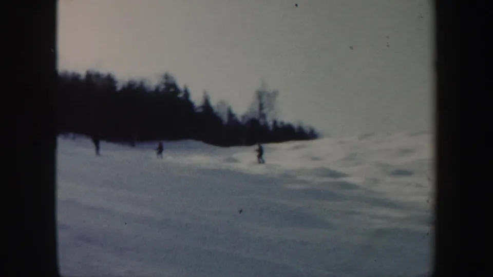 Small figures ski across a pale Vermont snow slope in a soft 1962 8mm home-movie frame.