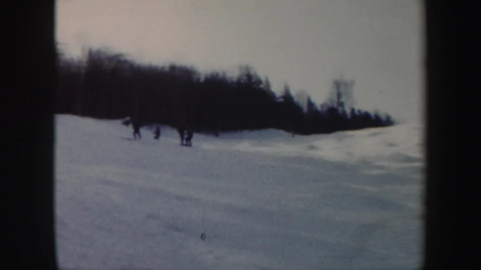 A small group of skiers gathers or passes on a snowy Vermont slope, filmed from a fixed 8mm home-movie viewpoint in 1962.