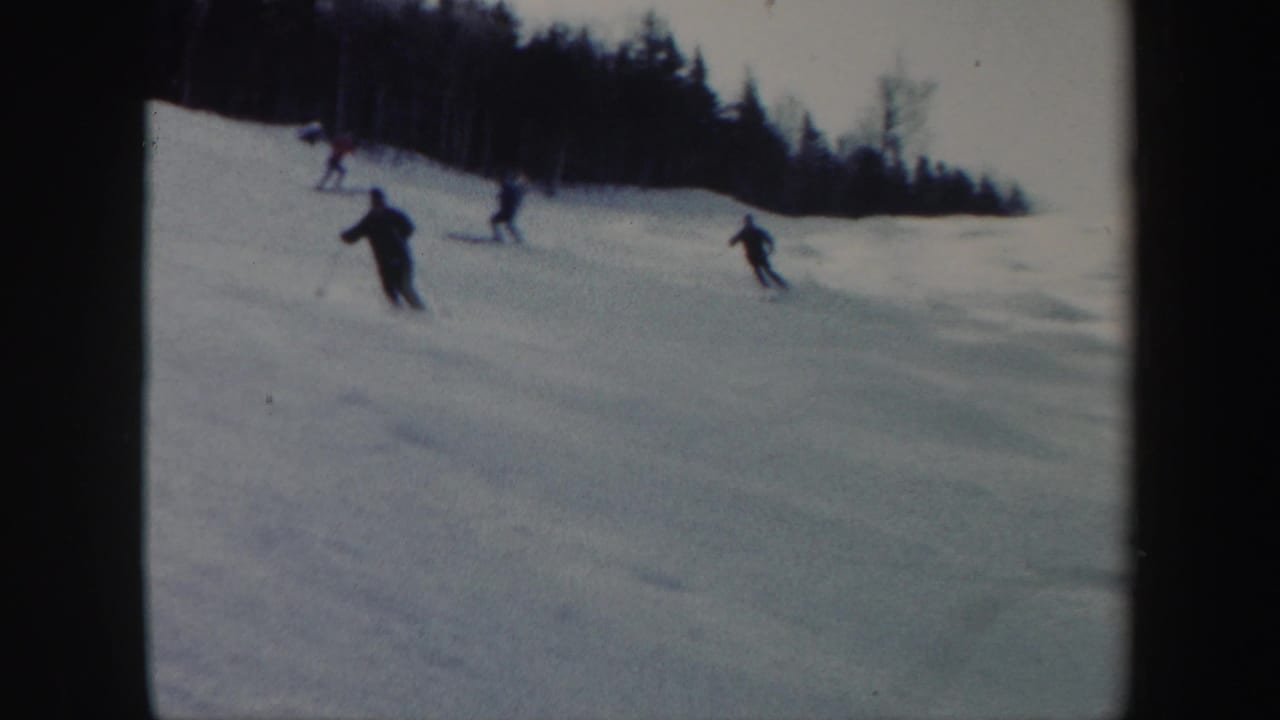 1962 Vermont ski footage frame with several distant skiers crossing a snowy hill under an overcast sky.