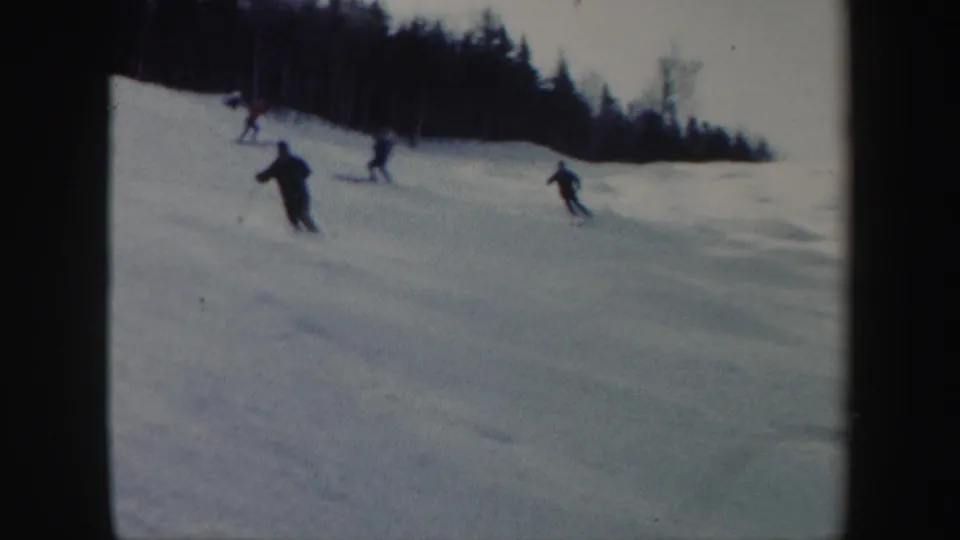 1962 Vermont ski footage frame with several distant skiers crossing a snowy hill under an overcast sky.