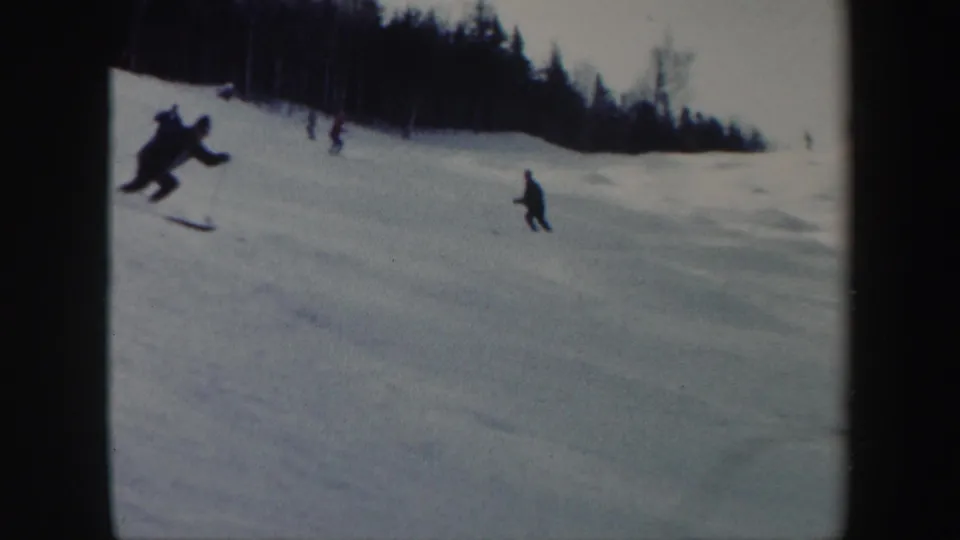 1962 Vermont home-movie frame with one skier close to the camera and others farther down the snowy slope.