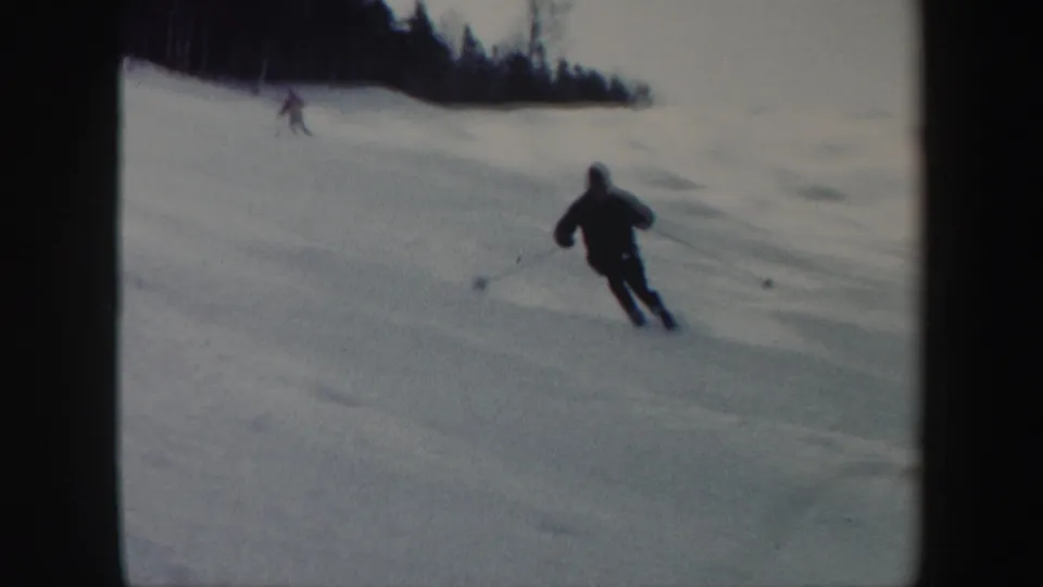 1962 Vermont frame showing a foreground skier turning downhill, with another skier and wooded slope in the background.