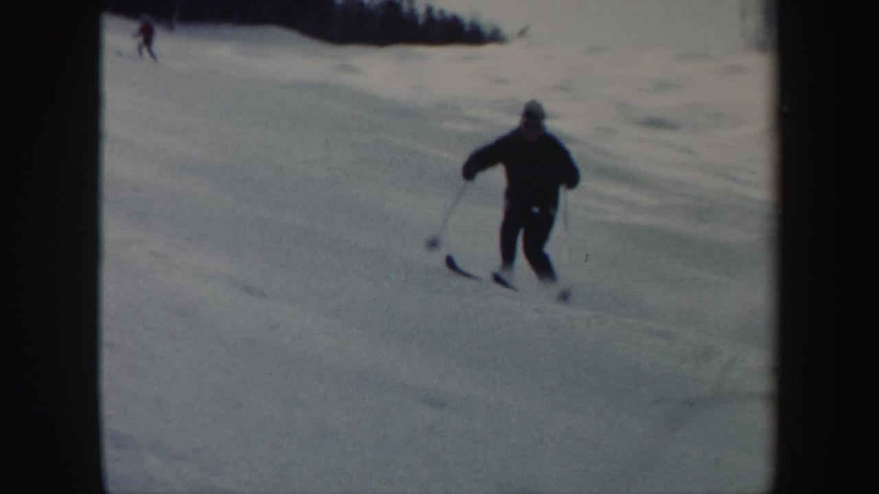 Skier in dark winter clothing descends a snowy slope with another skier in the distance.