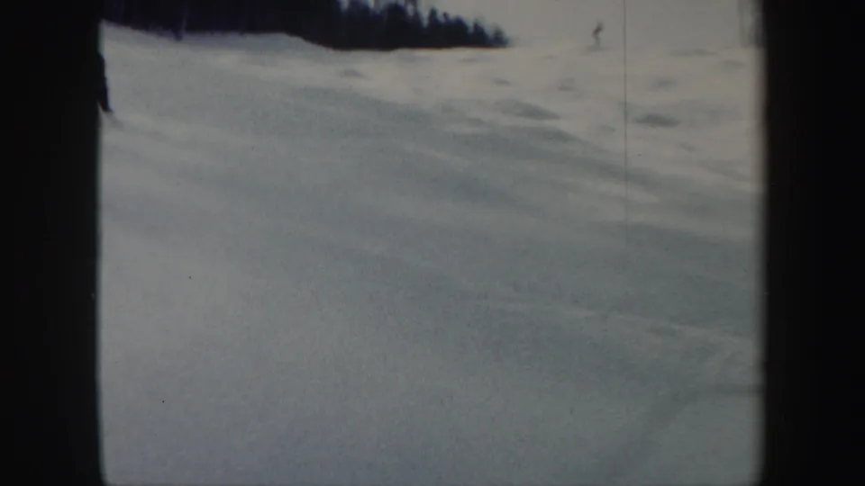 1962 Vermont 8mm frame showing an open snow-covered ski slope, a distant skier, and a dark tree line along the upper edge.