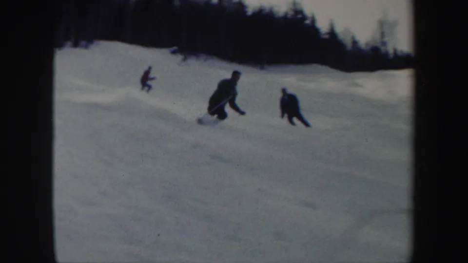1962 Vermont 8mm frame showing multiple skiers descending a snowy slope, with dark winter clothing and trees in the background.