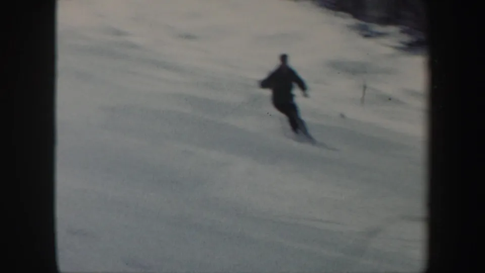 1962 Vermont 8mm frame showing a skier in dark clothing carving across a snowy slope, with muted color and soft focus.