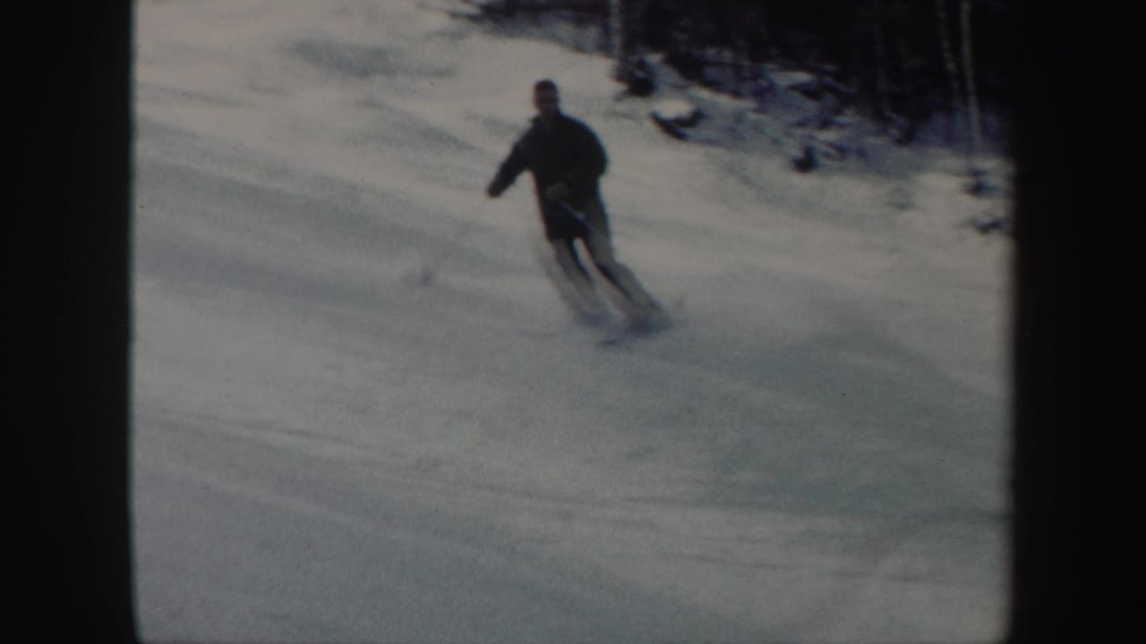 A skier in dark clothing turns across a snowy slope near a treeline.