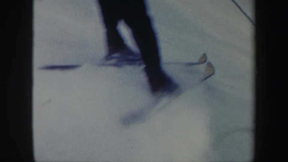 A close, blurred 8mm view shows a skier's lower body, skis, and poles passing across the snow in Vermont.