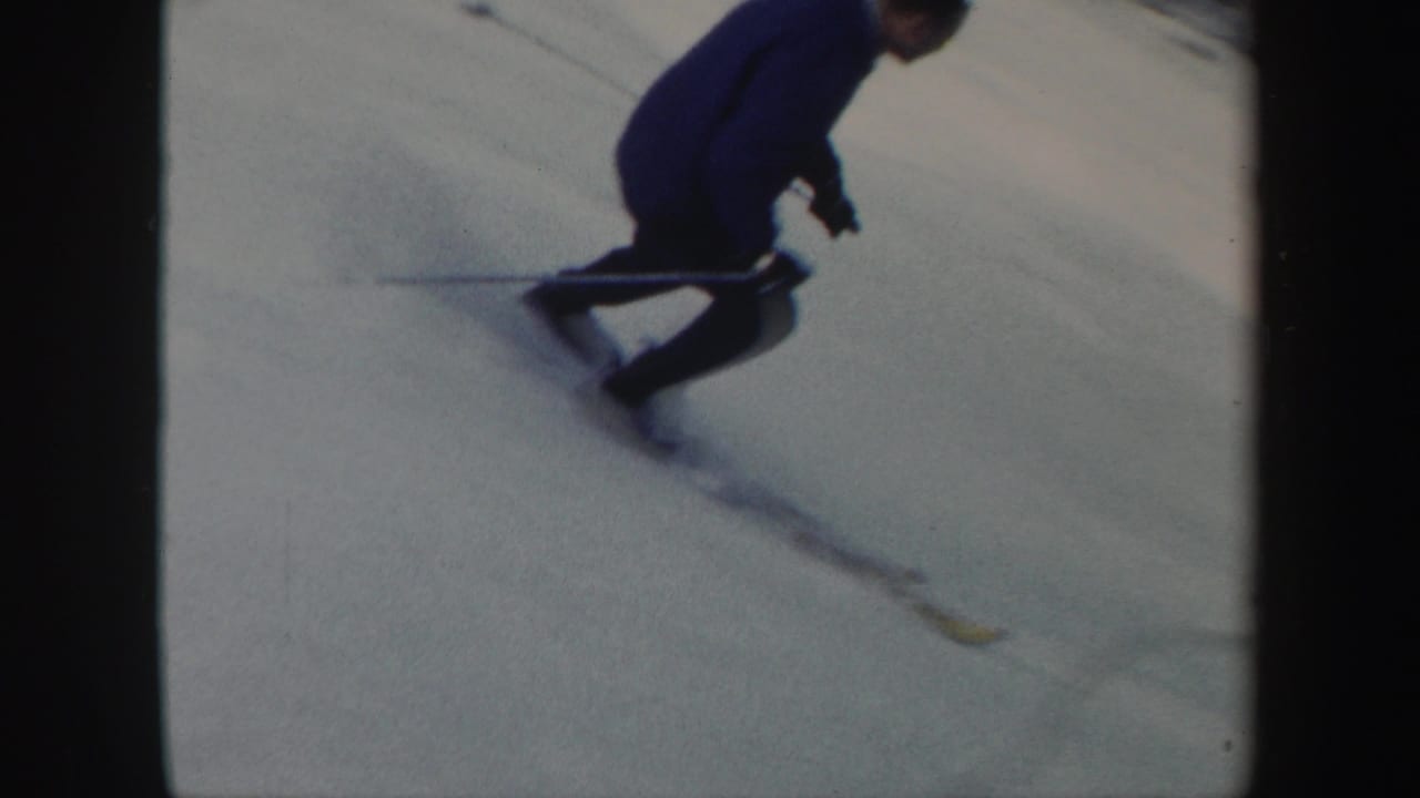 A skier in dark winter clothing carves across a snowy Vermont slope in 1962 home-movie footage.
