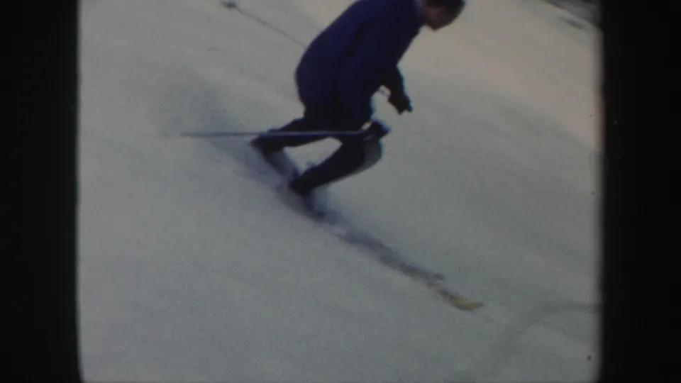 A skier in dark winter clothing carves across a snowy Vermont slope in 1962 home-movie footage.