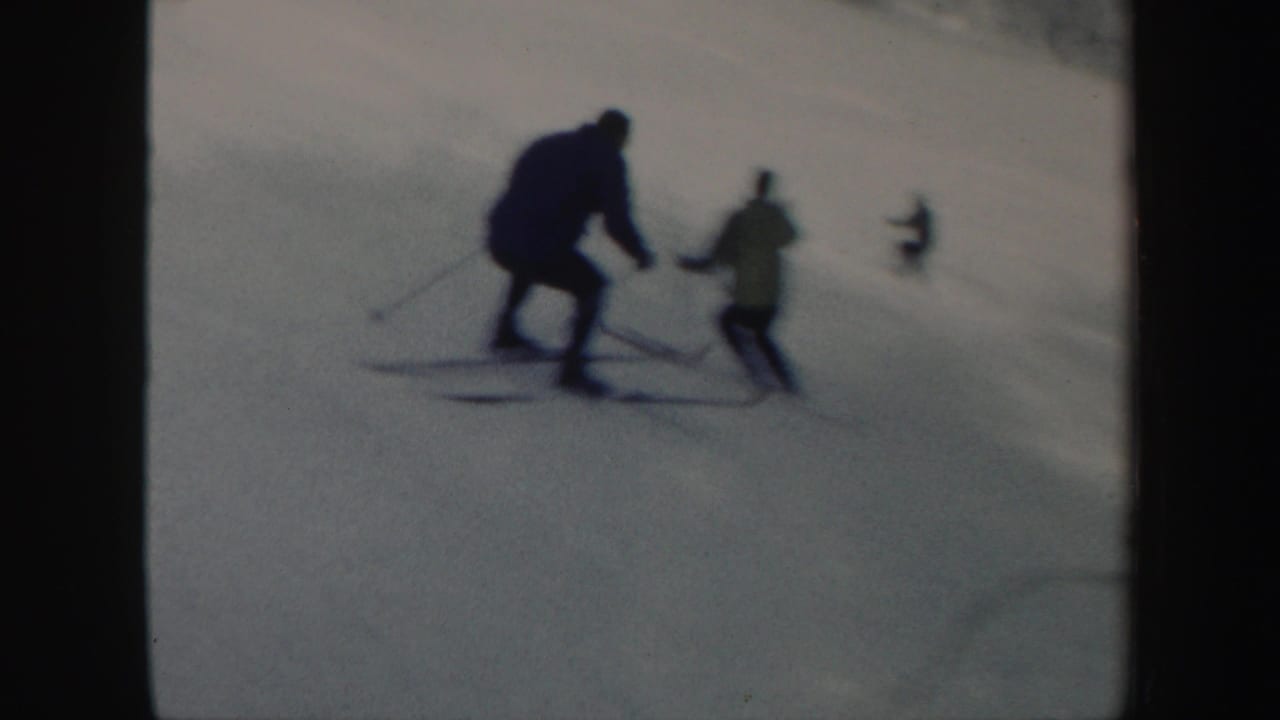 Two skiers descend a snowy Vermont slope, with a distant skier visible farther uphill in the 1962 8mm frame.