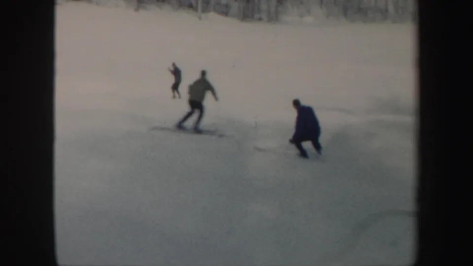 Multiple skiers are scattered across a snowy Vermont hillside, with a tree line behind them in 1962 home-movie footage.