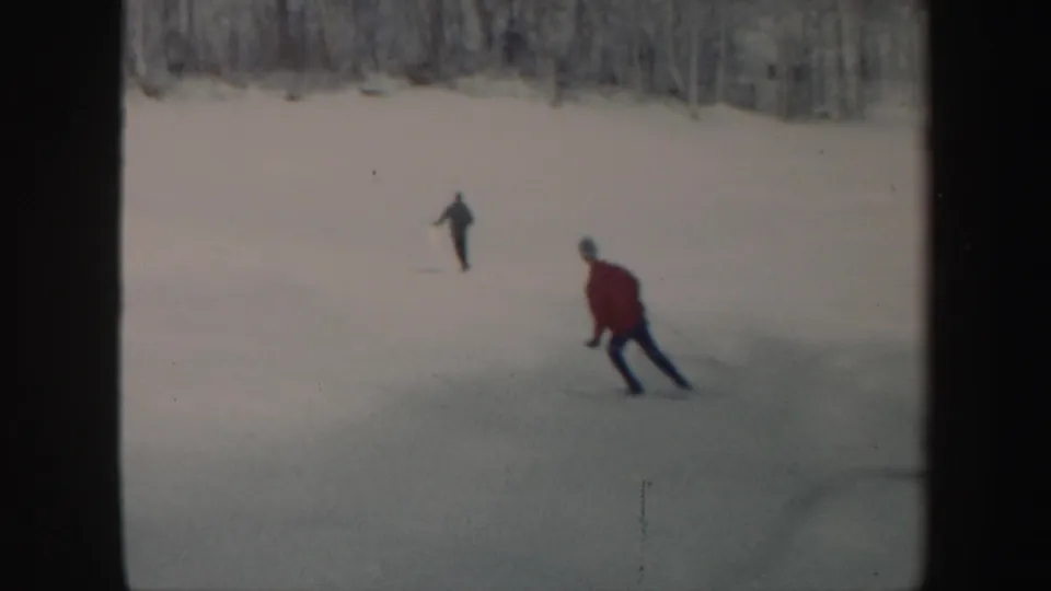 A skier in a red jacket cuts across the snowy Vermont slope while another skier appears in the distance.