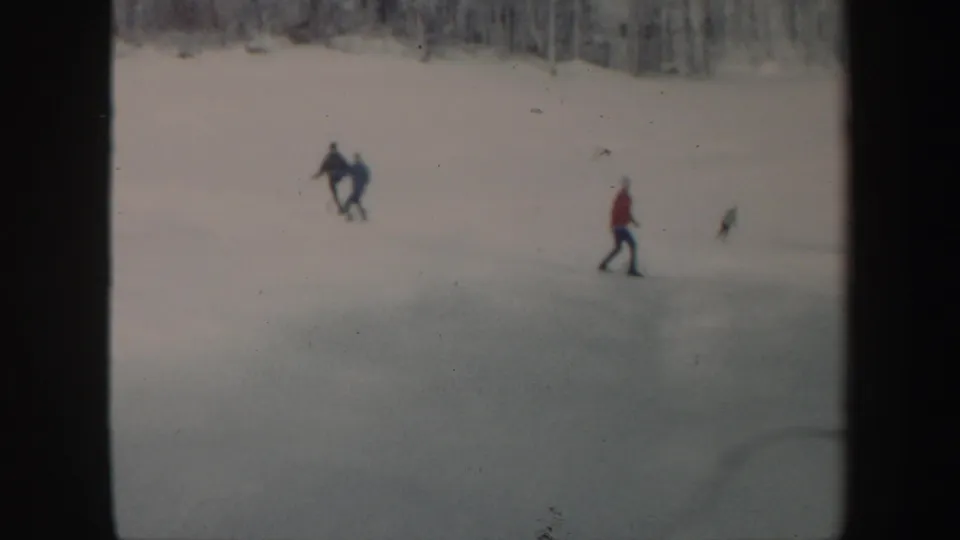 Distant skiers gather and move across the Vermont snow slope near bare winter trees.