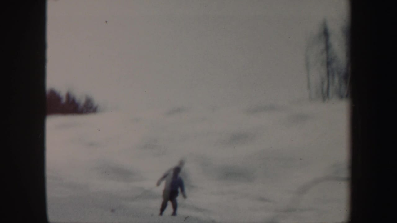 The skier continues downhill on a pale snowfield in the Vermont winter scene, filmed with soft 8mm focus.