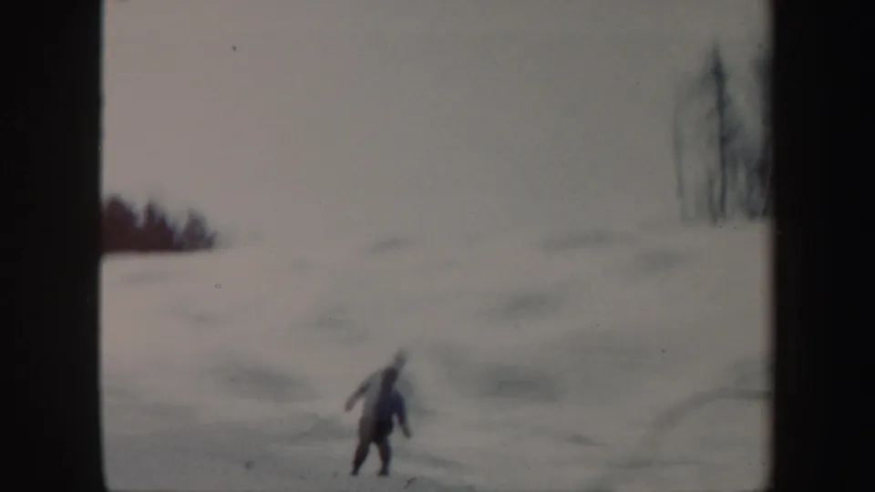 The skier continues downhill on a pale snowfield in the Vermont winter scene, filmed with soft 8mm focus.