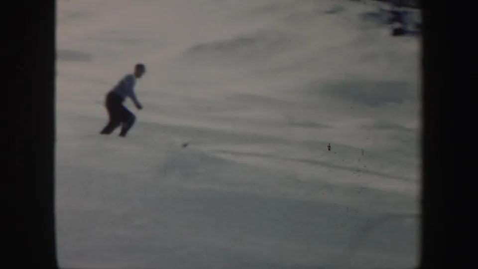 A skier in a blue shirt and dark pants bends slightly while skiing downhill in the 1962 Vermont home-movie clip.