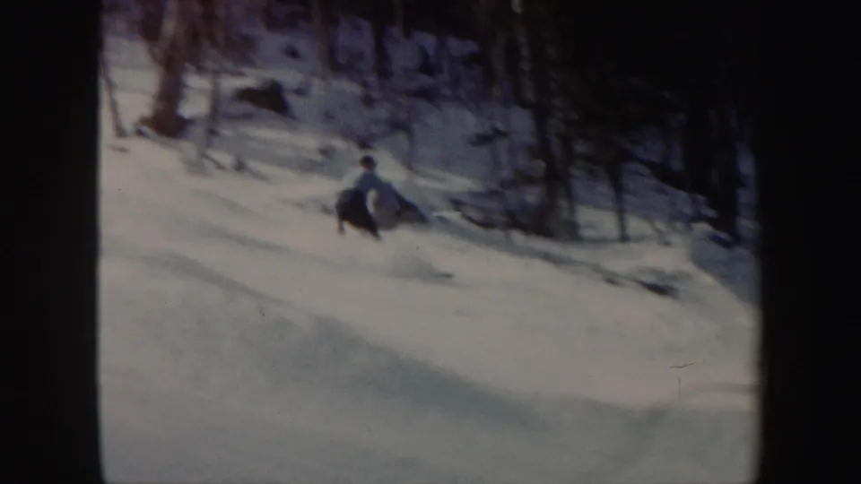 A skier in Vermont, 1962, descends a snowy wooded hillside in soft 8mm color footage.