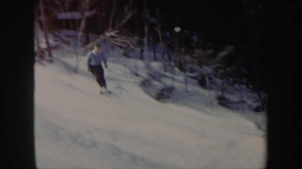 A closer view shows the skier in a light sweater and dark pants moving across the snowy Vermont hillside.