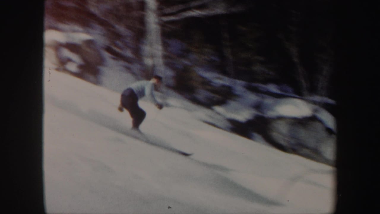 A skier in a light top and dark pants moves downhill on a snowy Vermont slope in 1962, with trees and rocks along the edge.
