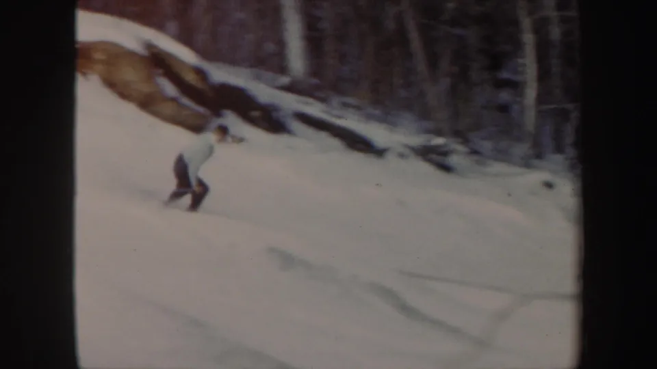 A skier leans forward while descending the Vermont snow slope, framed by dark woods, exposed rock, and 8mm contact-sheet borders.