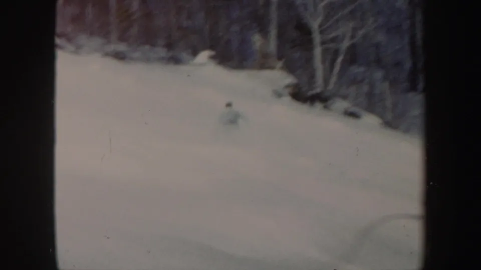 1962 Vermont 8mm frame showing a distant skier moving across a snowy hillside near leafless woods.