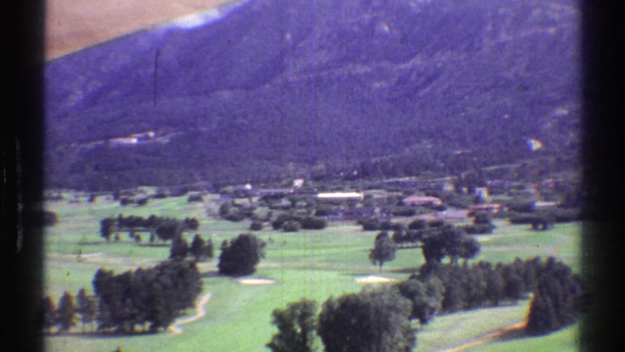 Green valley grounds with scattered trees and mountains in the background.