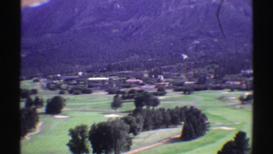 1969 Colorado 8mm view over a green valley with scattered trees, distant structures, and hazy mountains.