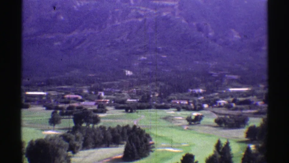 1969 Colorado frame showing landscaped green terrain, grouped trees, low valley buildings, and mountain foothills.