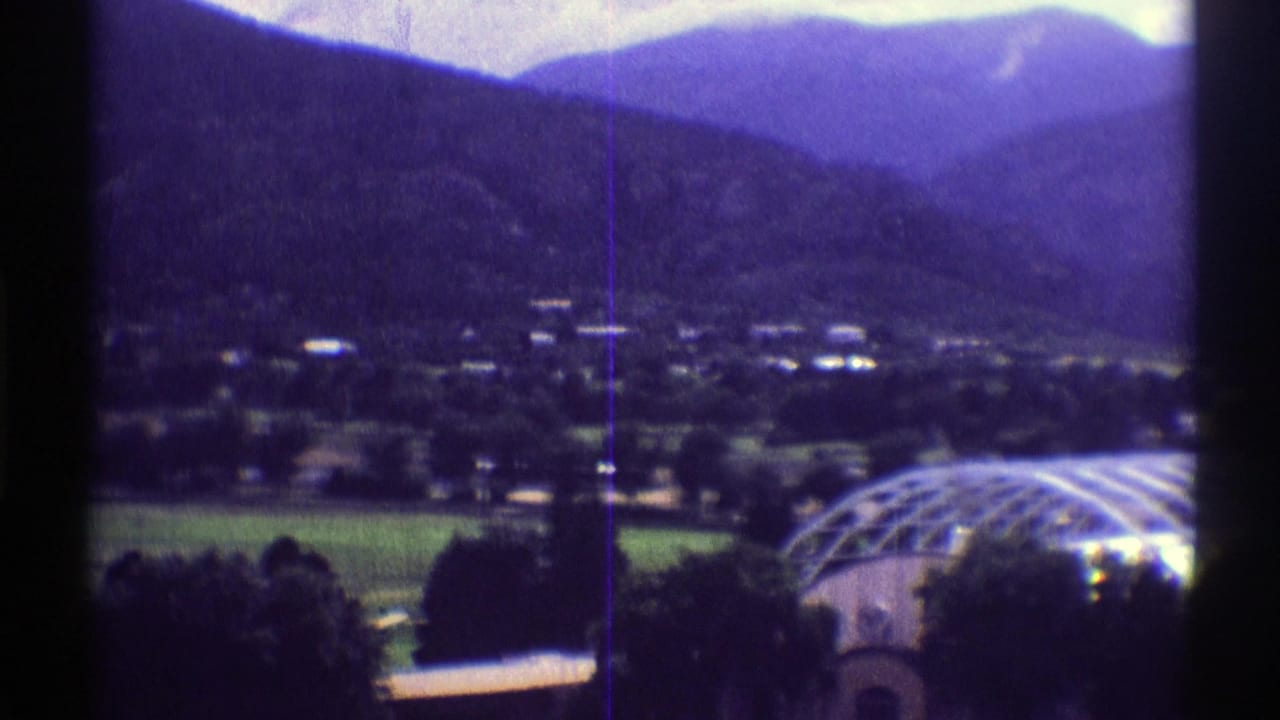 A Colorado mountain village appears across the valley in this 1969 8mm frame, with green fields and a curved greenhouse roof at lower right.