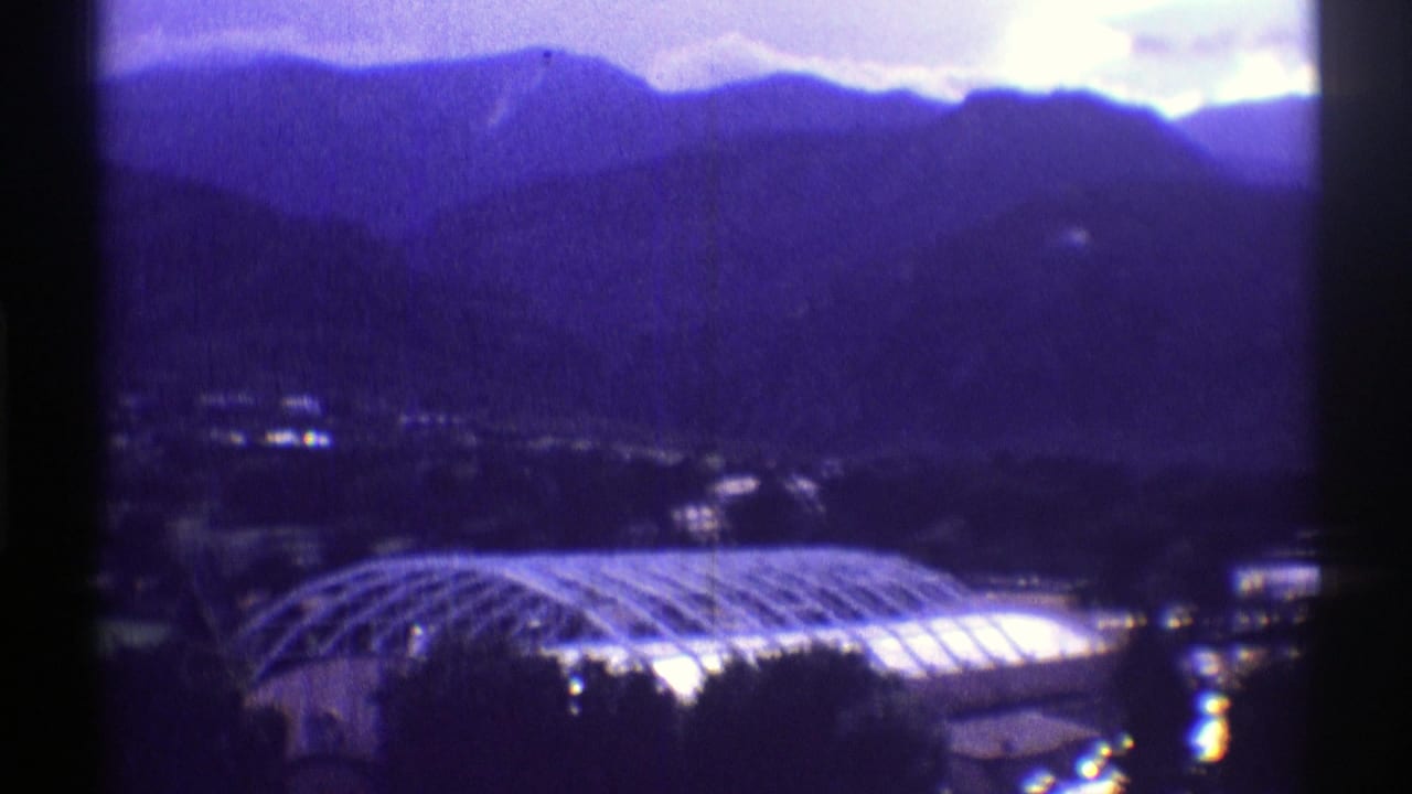 1969 Colorado 8mm frame showing layered mountains above a bright domed structure and dark foreground trees.