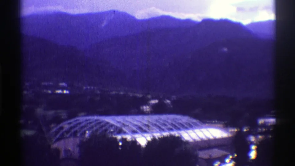 1969 Colorado 8mm frame showing layered mountains above a bright domed structure and dark foreground trees.